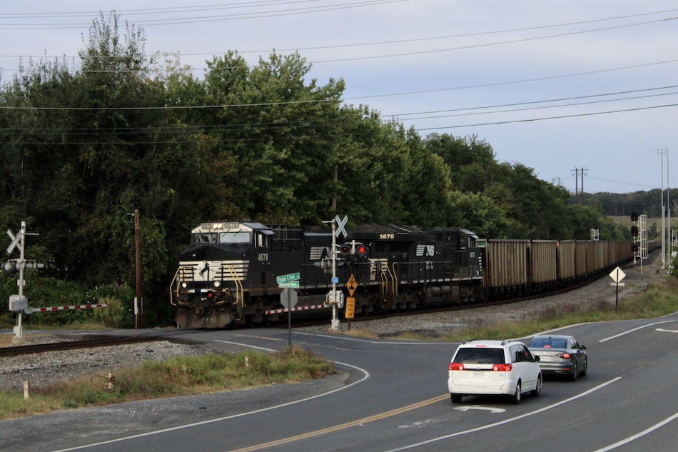 An empty coal train passes a gated road crossing