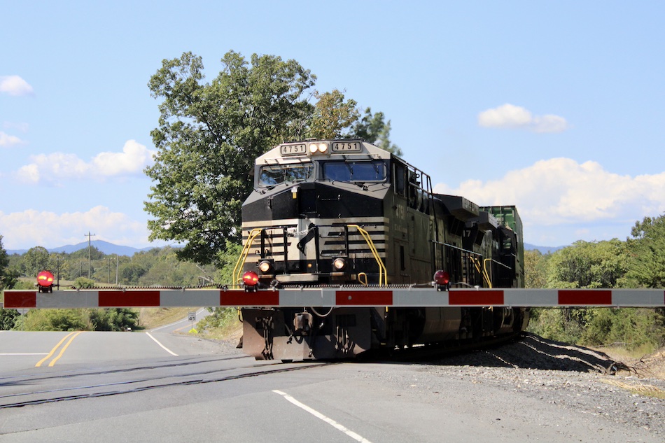 A train crosses a road behind a crossing gate on a beautiful day.