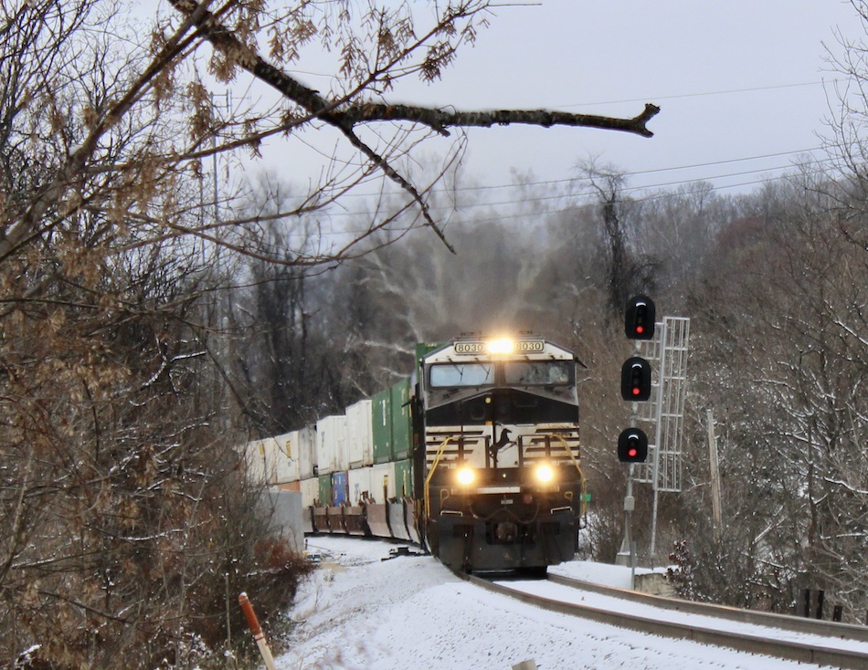A Norfolk Southern train carrying containers passes a signal tower after a snowfall.