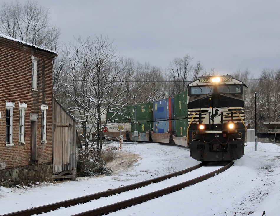 A Norfolk Southern train carrying containers passes a historic building after a snowfall