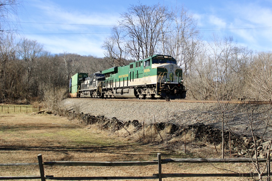 Norfolk Southern locomotive 8099 is painted in Southern Railway colors as it leads an intermodal train through the countryside.