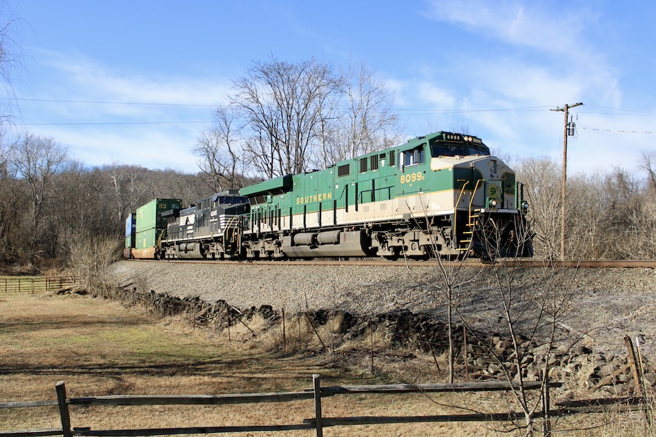 Norfolk Southern locomotive 8099 is painted in Southern Railway colors as it leads an intermodal train through the countryside.