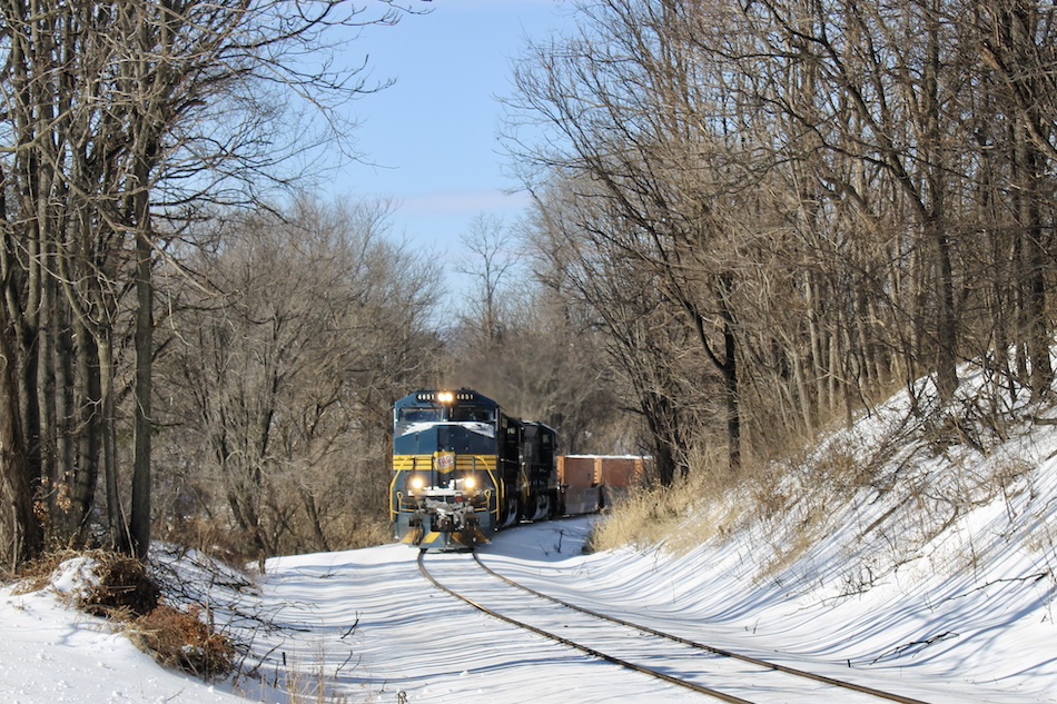 The railroad ties are not visible as they are covered from a recent snowfall as a train comes around the bend.