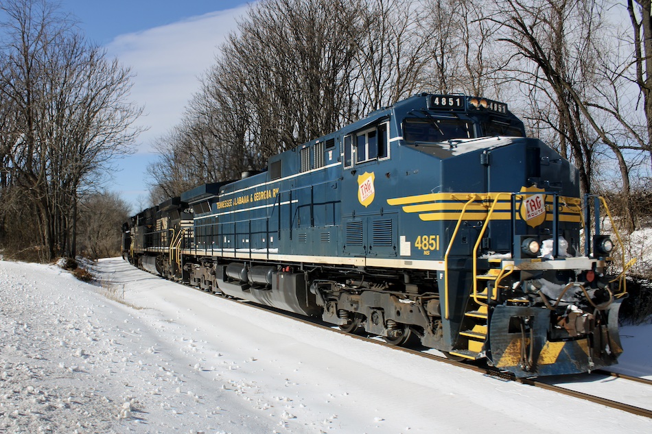 A blue and yellow locomotive painted in Tennessee, Alabama, and Georgia Railway livery leads a train.